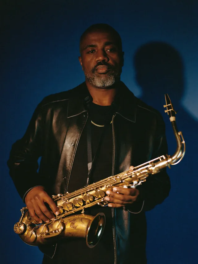 The AfrobeatMi saxophonist, alto sax held in both hands, black leather jacket.